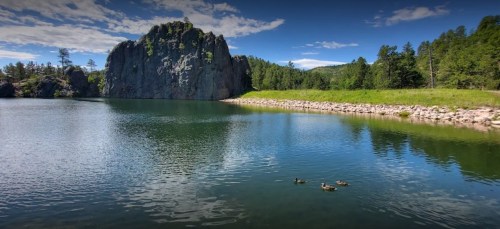 A serene lake surrounded by rocky cliffs and lush greenery, with ducks swimming peacefully in the water.
