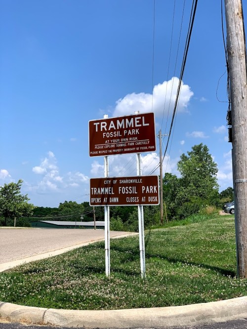 Sign for Trammel Fossil Park, indicating hours of operation and park rules, set against a clear blue sky.