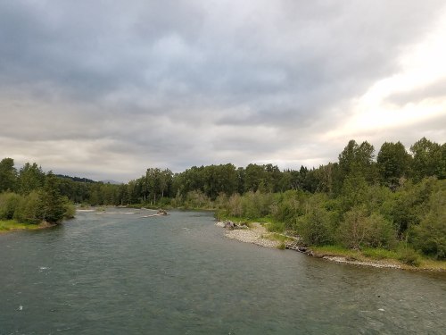 A serene river flows through a lush green landscape under a cloudy sky.