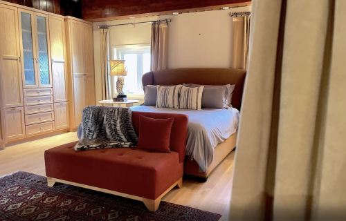 Cozy bedroom featuring a large bed, stylish bench, and warm wooden accents. Soft lighting creates a welcoming atmosphere.