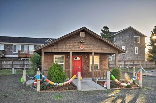 A cozy wooden house with a red door, surrounded by greenery and colorful decorations in a sunny outdoor setting.