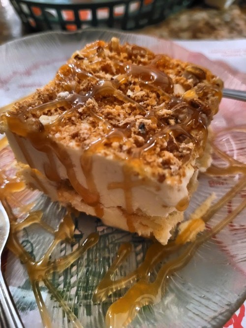 A slice of dessert drizzled with caramel sauce on a decorative plate, with a fork beside it.
