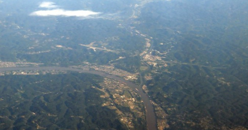 Aerial view of a winding river surrounded by green hills and a small town along the banks.
