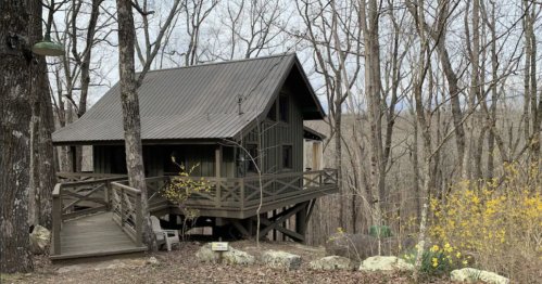A cozy cabin nestled among bare trees, with a wooden deck and a natural landscape in the background.
