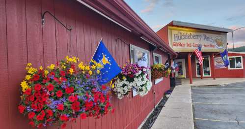 A red building with flower baskets and flags, featuring a sign for "The Huckleberry Patch" gift shop.