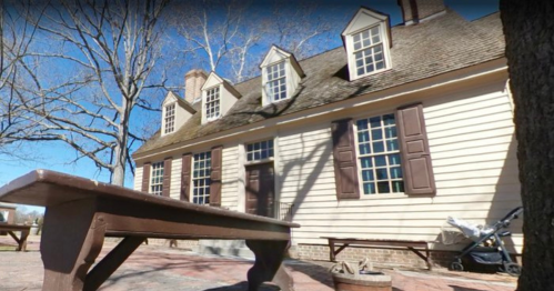 A historic building with multiple windows and a sloped roof, surrounded by trees and outdoor seating.