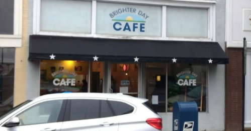 Exterior of Brighter Day Cafe with a black awning, open sign, and a parked white car in front.