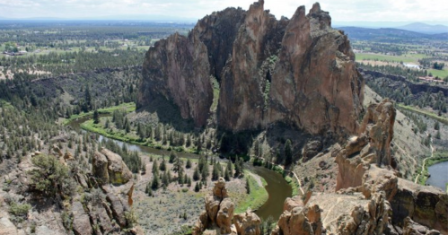Aerial view of a rocky formation surrounded by greenery and a winding river under a partly cloudy sky.