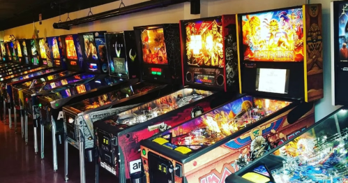 A row of colorful pinball machines lined up in a game arcade, featuring various themes and designs.
