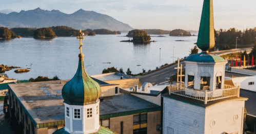 A scenic view of a waterfront with islands, featuring two church towers in the foreground and mountains in the background.