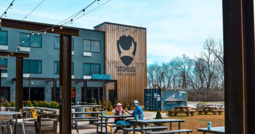 A modern building with a large logo, outdoor seating, and trees in the background on a clear day.