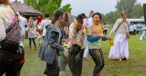 A group of people joyfully celebrating outdoors, covered in colorful powders during a festival.