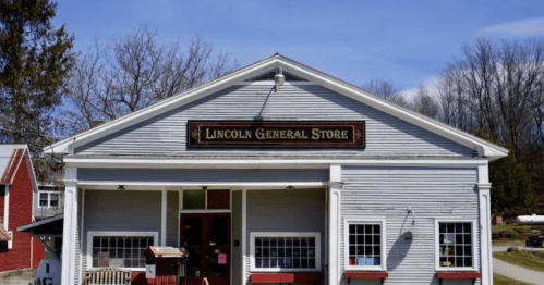 A quaint general store with a sign reading "Lincoln General Store," surrounded by trees and a clear blue sky.