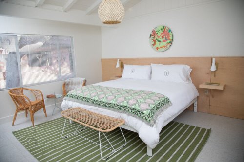 Bright, modern bedroom with a large bed, green patterned throw, wicker chair, and natural light from a window.