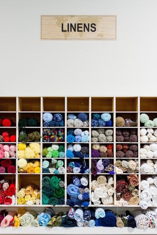 A neatly organized shelf labeled "LINENS" displaying various rolled fabrics in a range of colors.