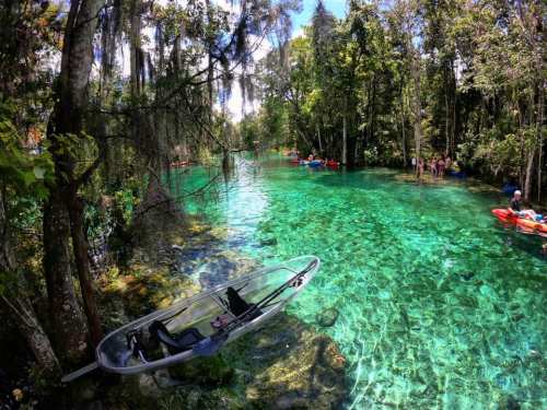 A serene, clear blue river surrounded by lush greenery, with kayakers enjoying the tranquil waters.
