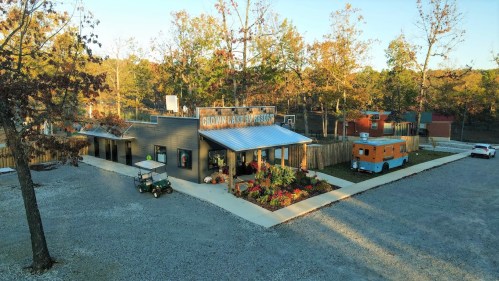 A rustic building with a sign reading "Gio's Rustic Cabin" surrounded by trees, a golf cart, and an orange food truck.