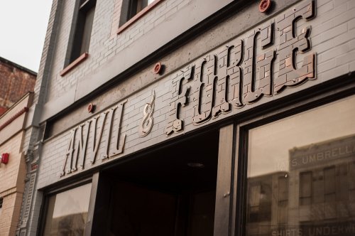 Close-up of a storefront sign reading "Anvil & Forge" with a vintage design on a brick building.