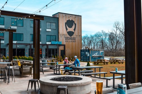 Outdoor seating area at DogHouse hotel, featuring picnic tables, a fire pit, and a large logo on the building.