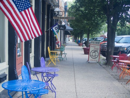 Colorful outdoor seating along a quiet street, with an American flag and a coffee shop sign in view.
