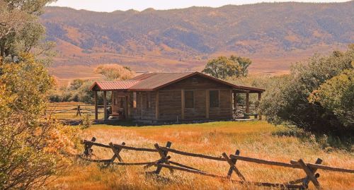 A rustic wooden cabin surrounded by colorful autumn foliage and mountains in the background.
