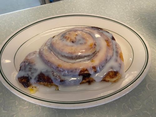 A freshly baked cinnamon roll drizzled with white icing on a white plate.