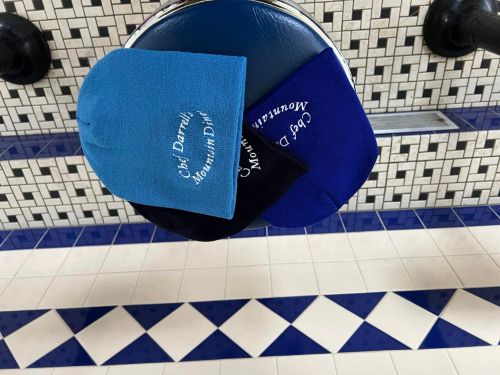 Three beanie hats in blue and black resting on a circular surface with a tiled background.