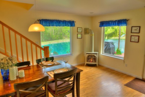 Cozy dining area with a wooden table, blue curtains, and a view of a serene outdoor space through large windows.