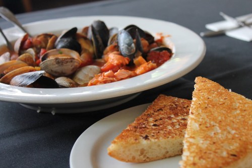 A plate of seafood with clams and mussels in a tomato sauce, accompanied by toasted bread on a white plate.