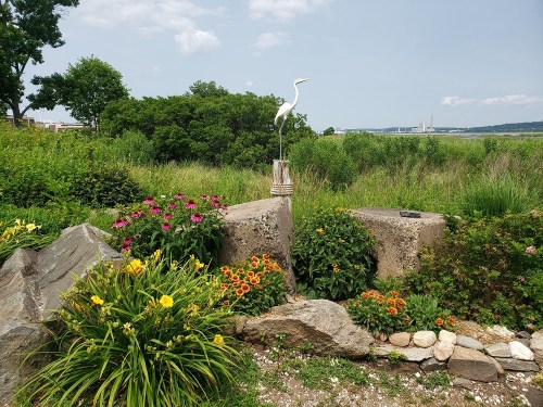 A serene garden scene featuring colorful flowers, rocks, and a white heron statue against a lush green backdrop.