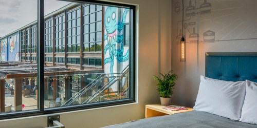 A cozy hotel room with a large window showcasing a mural of an octopus on a nearby building.
