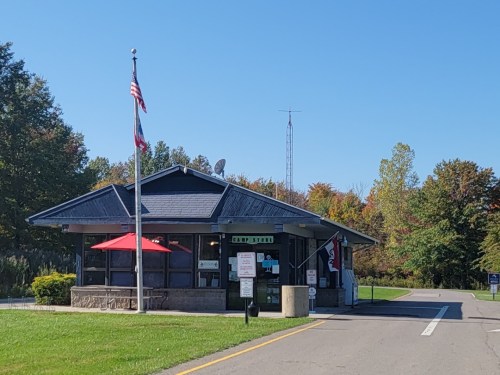 A small building with a flag, red umbrellas, and a sign, surrounded by trees and clear blue sky.