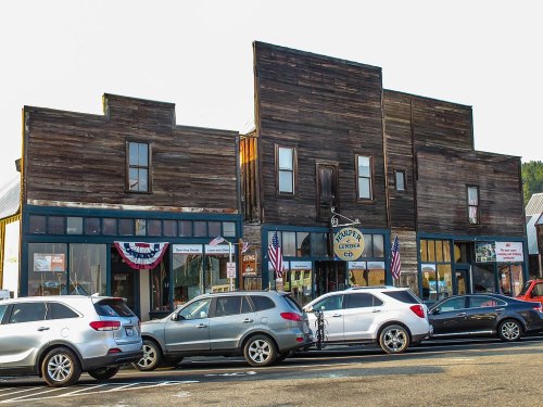 Historic wooden buildings with a sign for "Lumber Co," featuring parked cars and American flags.