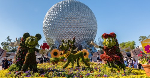 Mickey and Minnie Mouse topiaries with a dog in a flower garden, in front of the iconic Spaceship Earth at EPCOT.