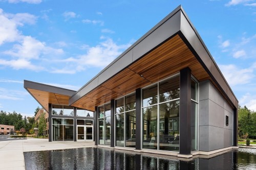 Modern building with large glass windows, wooden accents, and a reflecting pool in front, set against a blue sky.