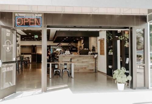 A cozy café entrance with an "OPEN" sign, featuring wooden decor and plants inside.