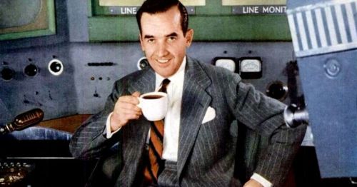A man in a suit smiles while holding a coffee cup, seated in a vintage broadcasting studio.