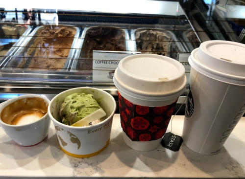 A small cup of espresso, a cup of green ice cream, and two coffee cups on a counter with gelato in the background.