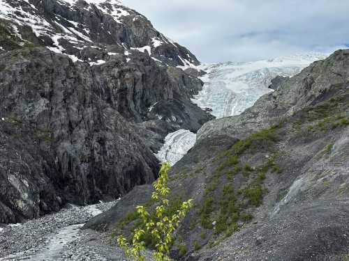 A glacier flows down a rocky mountain landscape, surrounded by snow-capped peaks and sparse greenery.