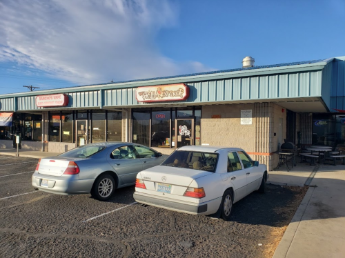 A storefront with large windows and a blue roof, featuring two parked cars in front and a clear sky above.