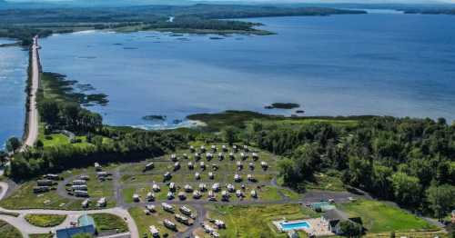 Aerial view of a lakeside RV park with numerous campers, a pool, and a scenic waterway in the background.