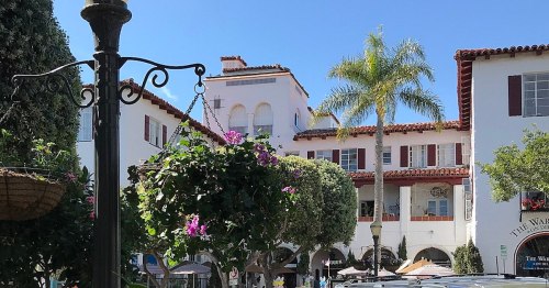 A sunny plaza with palm trees, hanging flower baskets, and Spanish-style buildings in the background.
