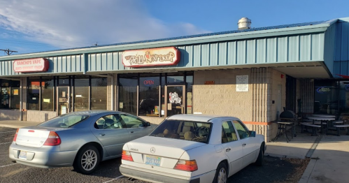 Exterior of a restaurant with a blue awning, large windows, and parked cars in front. Sign reads "Open."