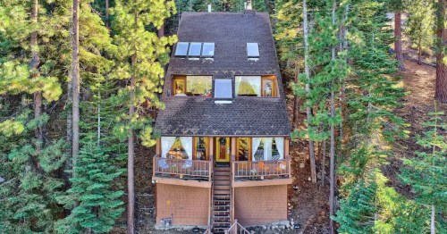A cozy cabin nestled among tall trees, featuring large windows and a welcoming porch.