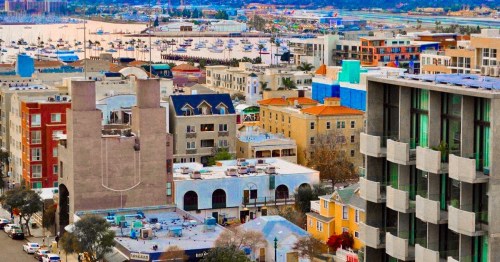 Aerial view of a coastal city with colorful buildings, marinas, and a waterfront in the background.