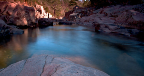 A serene river flows between rocky banks, surrounded by trees and a tranquil landscape.