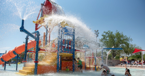 A colorful water play structure with slides and water sprays, filled with children enjoying a sunny day at a water park.