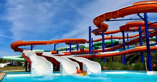 A water park scene featuring colorful water slides and a person on a float in a pool below.