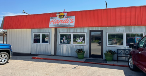 A small restaurant with a red roof and sign reading "Hlandi's" featuring a burger, surrounded by parked cars.