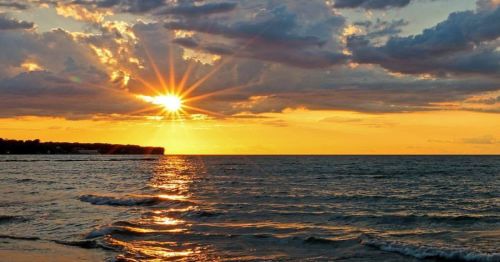 A vibrant sunset over the ocean, with golden rays shining through clouds and reflecting on the water's surface.